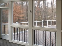 <b>Interior shot of a screened porch with composite deck boards, white composite railing and black aluminum balusters. Showing the handcrafted aluminum screen door as the exit onto the deck. All beams and supports are wrapped and a downward illuminated deck rail light is shown on one of the supports. Exterior posts have post cap lights to illuminate the night.</b>