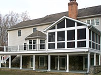<b>Screened Porch with a gable style roof, Screeneze and Super Screen Mesh, Composite deck boards with white vinyl railing and black aluminum balusters. The entire deck is wrapped with white fascia board, and the support beams and posts are also wrapped in vinyl. Dek Drain under-deck drainage system keeps rain, spills and snow melt from dripping through the decking boards above, creating a dry useable room below.</b>