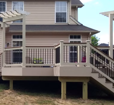 Composite deck with tan vinyl railing, matching cocktail rail, black balusters, and two tan trellis.