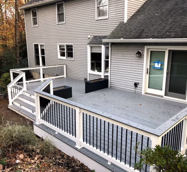 Trex Select Pebble Gray Decking with White Lincoln Vinyl Railing, Round Black Aluminum Balusters, matching Pebble Gray Cocktail Rail, and two Composite Planters