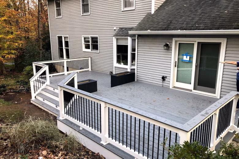 Trex Select Pebble Gray Decking with White Lincoln Vinyl Railing, Round Black Aluminum Balusters, matching Pebble Gray Cocktail Rail, and two Composite Planters